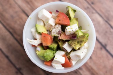Avokado, domates ve beyaz kasede servis edilen taze mozzarella peynirli taze sebzelerden sağlıklı salata.