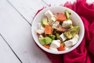 Avokado, domates ve beyaz kasede servis edilen taze mozzarella peynirli taze sebzelerden sağlıklı salata.
