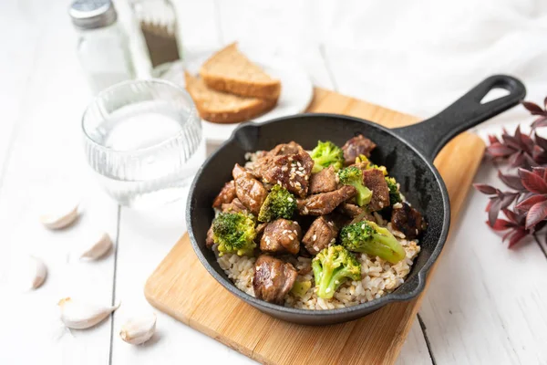 Beef and broccoli over rice in a black skillet topped with sesame seeds