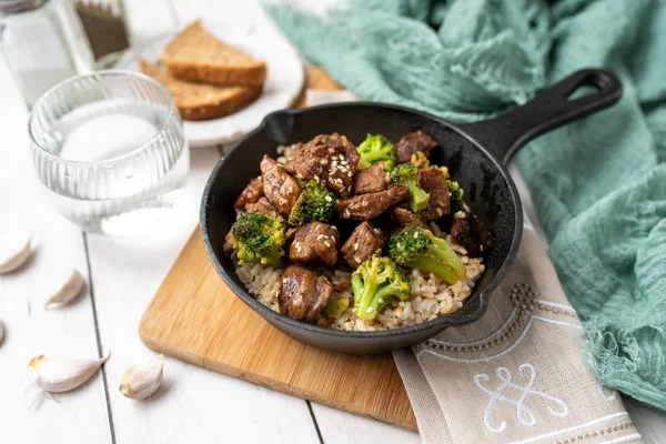 Beef and broccoli over rice in a black skillet topped with sesame seeds