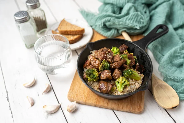 Beef and broccoli over rice in a black skillet topped with sesame seeds