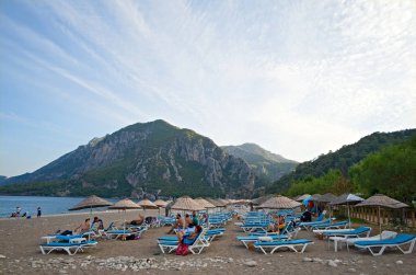 Cirali, Antalya, Türkiye - Eylül 2018: Cirali Sahili 'nde güneşlenen insanlar. Arkaplanda dağlar ve mavi gökyüzü.