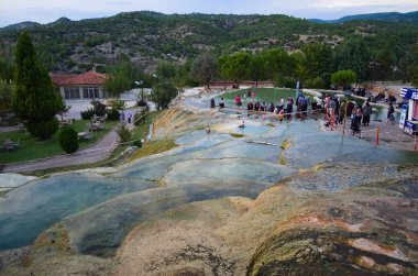Karahayit, Pamukkale / Denizli, Türkiye - Eylül 2018: Kırmızı travertin teraslarda temiz sıcak su. Kaplıcaların manzarası. Türk turistler sağlık için banyo yapıyor ve termal su içiyor.