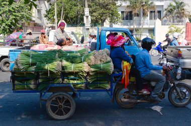 Phnom Penh, Kamboçya - Mart 2015: Motosikletin arkasındaki faytonda yeşil soğan yığını. Çiftçiler şehir trafiği sıkışıklığında soğan yığınıyla çiftçi pazarına gidip hasatını satıyorlar..