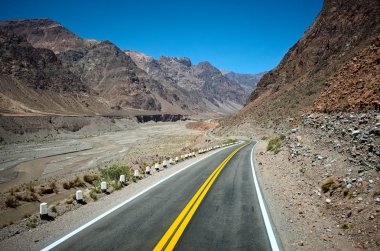 And Dağları 'ndaki karayolu kanyon nehri boyunca. Kurak iklimde kayalık arazili çöl gibi boş bir yol. Arjantin 'in Mendoza eyaletindeki dağların arasından geçen sarı çizgili virajlı yol.