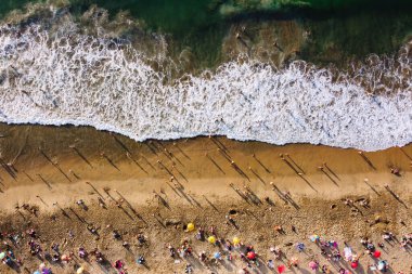 Banyo yapan insanlarla dolu bir sahilin kuş bakışı görüntüsü. Güneşli bir günde okyanus kenarındaki kumsalda şemsiyesiz dinlenen insanlar. Playa Caleta Portales 'in hava görüntüsü. Valparaiso, Şili.