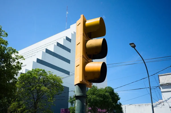 Yellow traffic light close up against buildings and blue sky on the street.