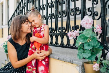 Sevimli küçük kızını sarılma mutlu bir genç kadın. Güzel gülümseyen kız annesiyle sokakta