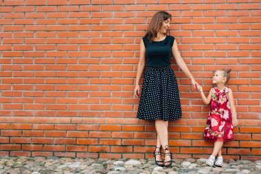 Moda aile kavramı - şık anne ve çocuk. Mutlu bir aile portresi: Tuğla duvara yakın duran küçük şirin neşeli kızı olan güzel bir kadın.