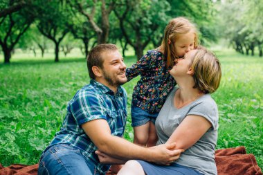Üç battaniye parkta eğleniyor yatan genç mutlu aile. Mutlu anne-babalık kavramı. Küçük kız öpüşme anne.