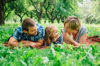 Üç battaniye parkta eğleniyor yatan genç mutlu aile. Mutlu anne-babalık kavramı. Annem ve babam açık havada küçük kızla