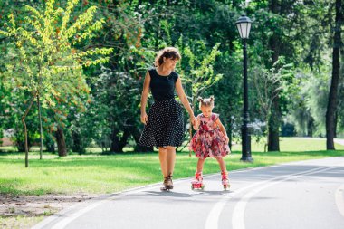 Anne Silindirler binmek için öğretim kızı. Neşeli genç kadın ve sevimli küçük kızını parkta paten binmek. Mutlu anne-babalık kavramı.