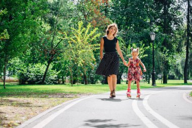 Anne Silindirler binmek için öğretim kızı. Neşeli genç kadın ve sevimli küçük kızını parkta paten binmek. Mutlu anne-babalık kavramı.