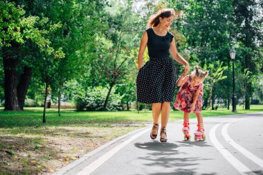 Anne Silindirler binmek için öğretim kızı. Neşeli genç kadın ve sevimli küçük kızını parkta paten binmek. Mutlu anne-babalık kavramı.
