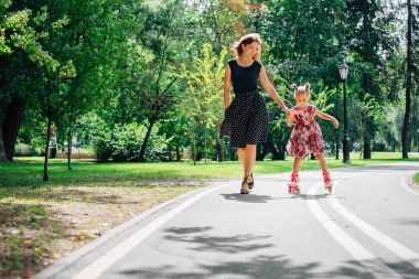 Anne Silindirler binmek için öğretim kızı. Neşeli genç kadın ve sevimli küçük kızını parkta paten binmek. Mutlu anne-babalık kavramı.