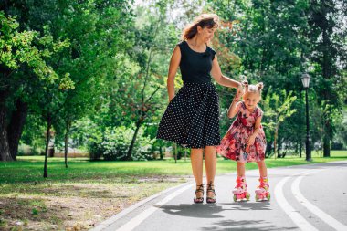 Anne Silindirler binmek için öğretim kızı. Neşeli genç kadın ve sevimli küçük kızını parkta paten binmek. Mutlu anne-babalık kavramı.