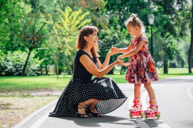 Anne Silindirler binmek için öğretim kızı. Neşeli genç kadın ve sevimli küçük kızını parkta paten binmek. Mutlu anne-babalık kavramı.