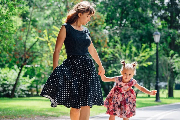 Anne Silindirler binmek için öğretim kızı. Neşeli genç kadın ve sevimli küçük kızını parkta paten binmek. Mutlu anne-babalık kavramı.