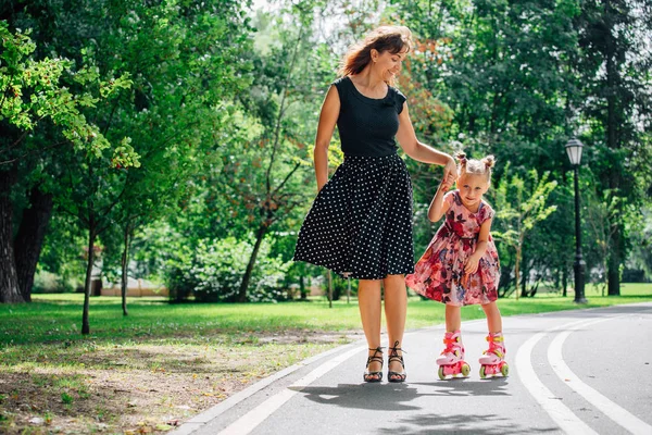 Anne Silindirler binmek için öğretim kızı. Neşeli genç kadın ve sevimli küçük kızını parkta paten binmek. Mutlu anne-babalık kavramı.