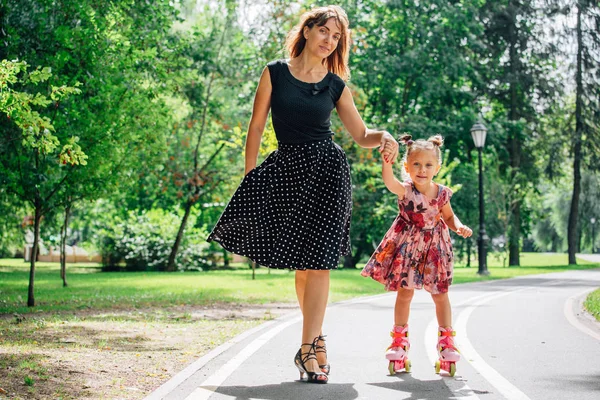 Anne Silindirler binmek için öğretim kızı. Neşeli genç kadın ve sevimli küçük kızını parkta paten binmek. Mutlu anne-babalık kavramı.