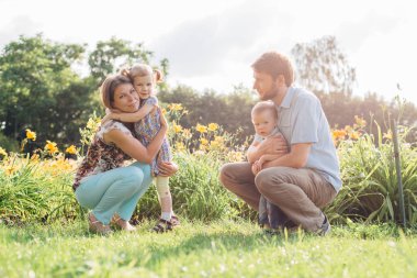 Genç mutlu aile açık havada çiçekler eğleniyor. İki sevimli çocukları tutarak aşık. Anne baba kız oğul.