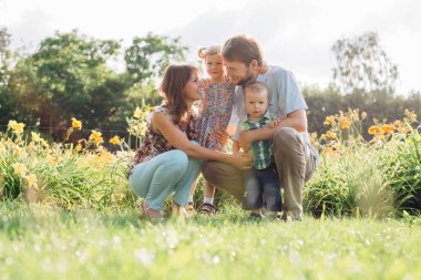 Genç mutlu aile açık havada çiçekler eğleniyor. İki sevimli çocukları tutarak aşık. Anne baba kız oğul.