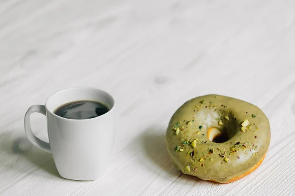 Cup of coffee and glazed almond donut on light wooden background.