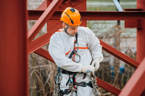 Industrial climber in uniform and helmet preparing rope and equipment for work. Professional worker getting ready for his risky job.
