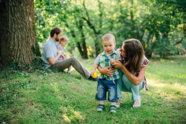 Parkta yürümeyi öğrenme şirin küçük oğlu. Mutlu anne gülen oğlu izlerken.