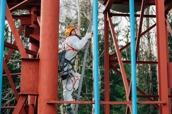 Industrial climber in uniform and helmet working on height outdoors. Professional worker climbing upstairs on water tower.