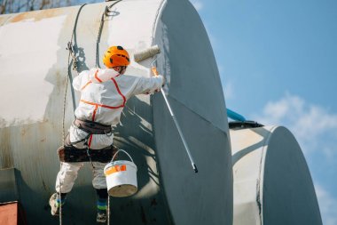 Endüstriyel dağcı kask ve Tekdüzen resim su kulesi. Profesyonel ressam yükseklik üzerinde çalışıyor. Riskli iş. Aşırı işgal.