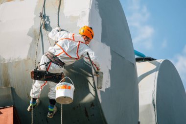 Endüstriyel dağcı kask ve Tekdüzen resim su kulesi. Profesyonel ressam yükseklik üzerinde çalışıyor. Riskli iş. Aşırı işgal.