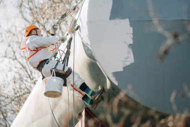 Endüstriyel dağcı kask ve Tekdüzen resim su kulesi. Profesyonel ressam yükseklik üzerinde çalışıyor. Riskli iş. Aşırı işgal.