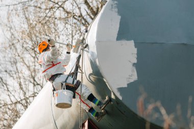 Endüstriyel dağcı kask ve Tekdüzen resim su kulesi. Profesyonel ressam yükseklik üzerinde çalışıyor. Riskli iş. Aşırı işgal.