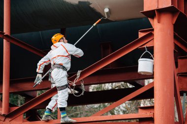 Endüstriyel dağcı kask ve Tekdüzen resim su kulesi. Profesyonel ressam yükseklik üzerinde çalışıyor. Riskli iş. Aşırı işgal.