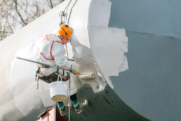 Industrial climber in helmet and uniform painting water tower. Professional Painter working on height. Risky job. Extreme occupation.