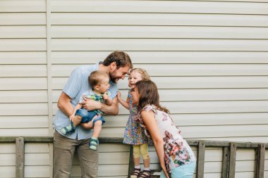 Evin duvarının yakınında genç mutlu aile ayakta. Eğlenmek ve oyun. Gülümseyen ve gülüyor. Güzel kadın ve erkek oğlu ve kızı ile