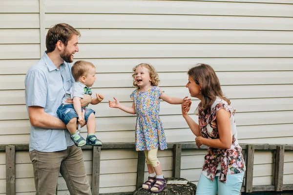 Young happy family standing near house wall. Having fun and playing. Smiling and laughing. Pretty woman and man with son and daughter