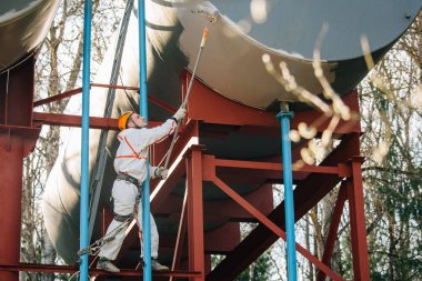 Endüstriyel dağcı kask ve Tekdüzen resim su kulesi. Profesyonel ressam yükseklik üzerinde çalışıyor. Riskli iş. Aşırı işgal.