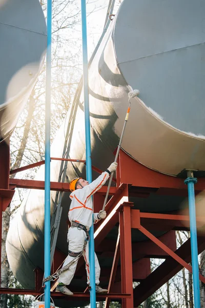 Industrial climber in helmet and uniform painting water tower. Professional Painter working on height. Risky job. Extreme occupation.