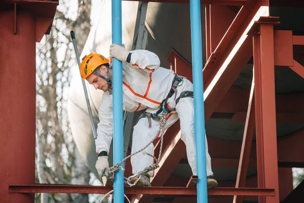 Industrial climber in helmet and uniform painting water tower. Professional Painter working on height. Risky job. Extreme occupation.