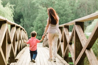 Annemin tatlı oğluyla yaz parkındaki tahta köprüde yürüyüşünün arka planı. Mutlu kadın ve neşeli küçük çocuk dışarıda