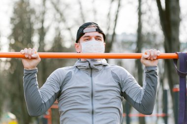 Sağlık maskeli genç adam barfiks çekiyor. Koronavirüs salgını sırasında eğitim.