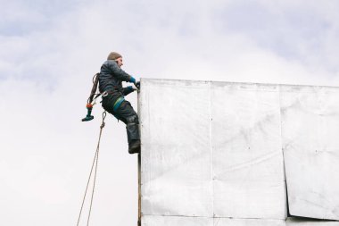 Endüstriyel tırmanış tamiri reklam panosu. Riskli bir iş. Yükseklik üzerinde çalış. Metal yapı. Elektrikli tornavida.