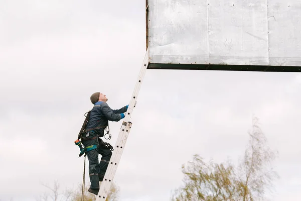 Industrial climber going up the ladder to the billboard. Risky job. Work on height