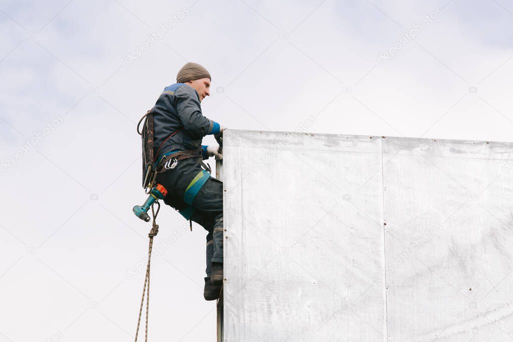 Industrial climber repair billboard. Risky job. Work on height. Metal construction. Electric screwdrive.