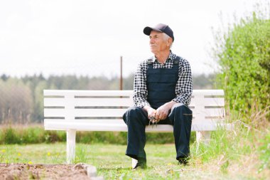 Gülümseyen kıdemli bahçıvan bahçede bankta oturuyor. Yaşlı adam işten sonra dinleniyor..