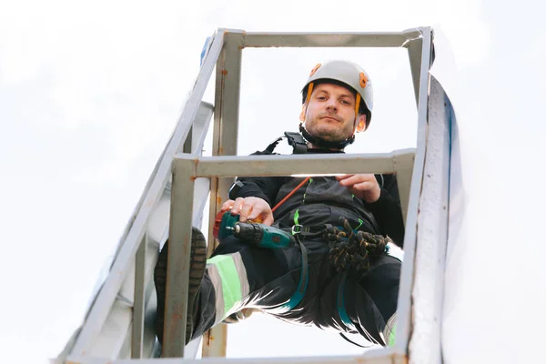 Portrait of Industrial climber in helmet and overall working on height. Risky job. Bottom view