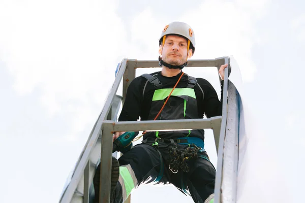 Portrait of Industrial climber in helmet and overall working on height. Risky job. Bottom view