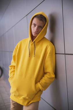 Sarı kapüşonlu ciddi bir genç, gri bir duvara karşı parlak elbiseli şık bir moda adamı.